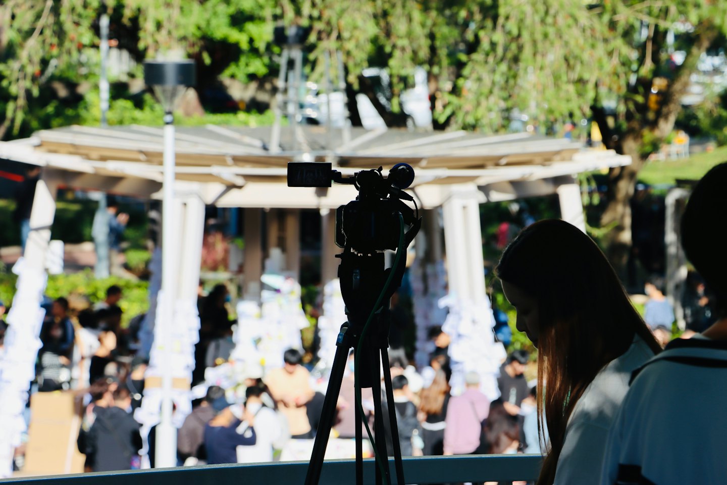 Una videocamera registra una riunione all'aperto sotto un gazebo.