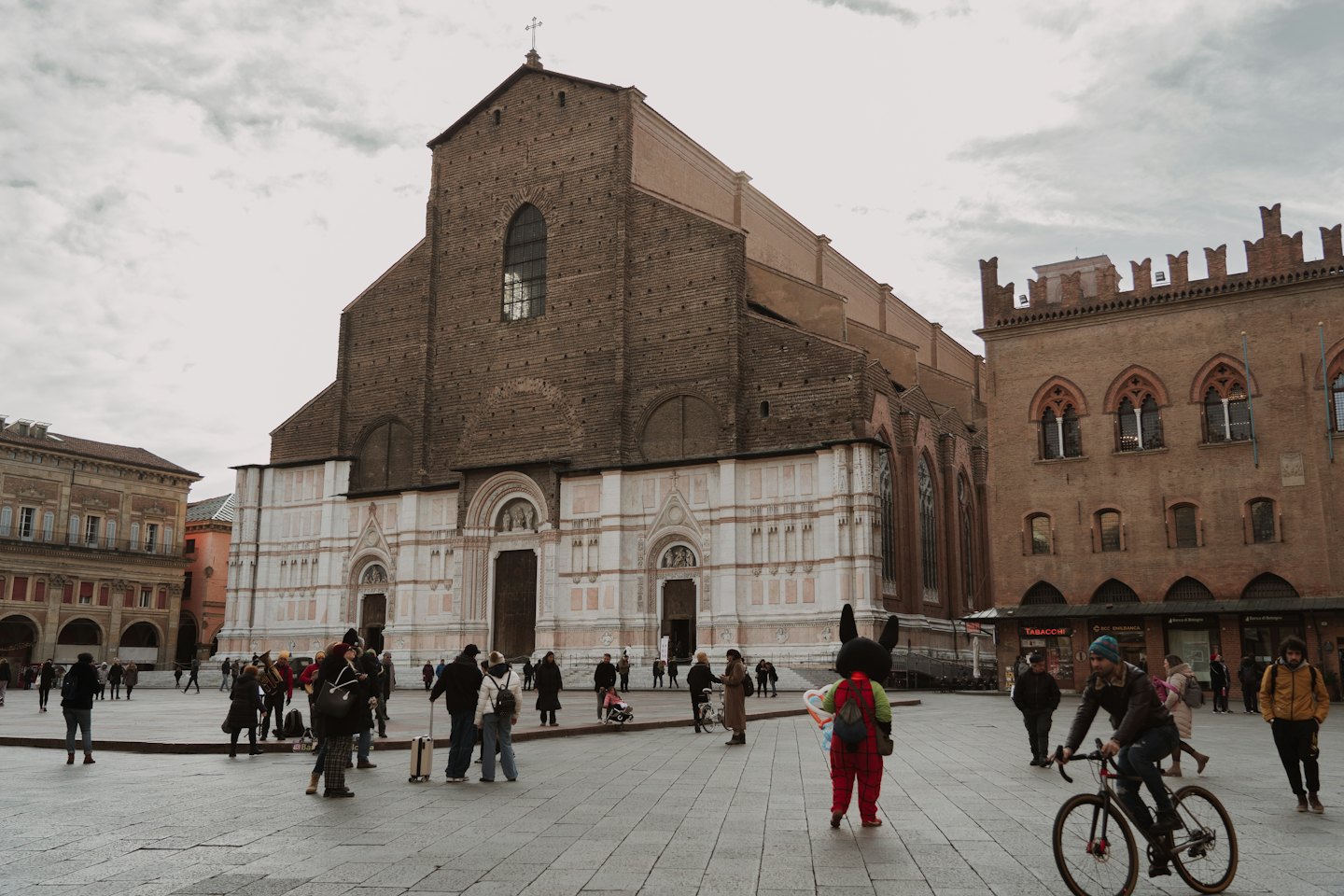 Persone attraversano una piazza cittadina vicino a una storica basilica in mattoni.